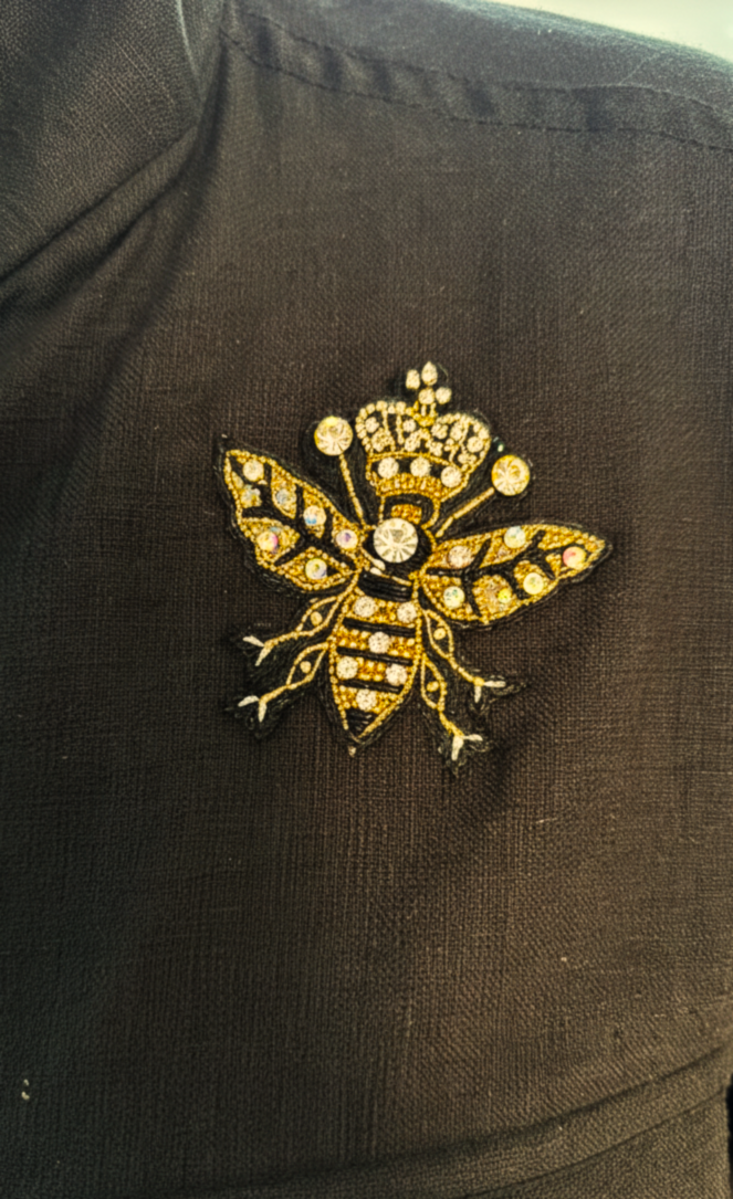 Close-up of a jeweled bee brooch on a black shirt, featuring intricate details and sparkling embellishments.